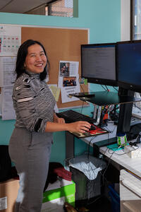 A smiling woman stands at a computer in an office