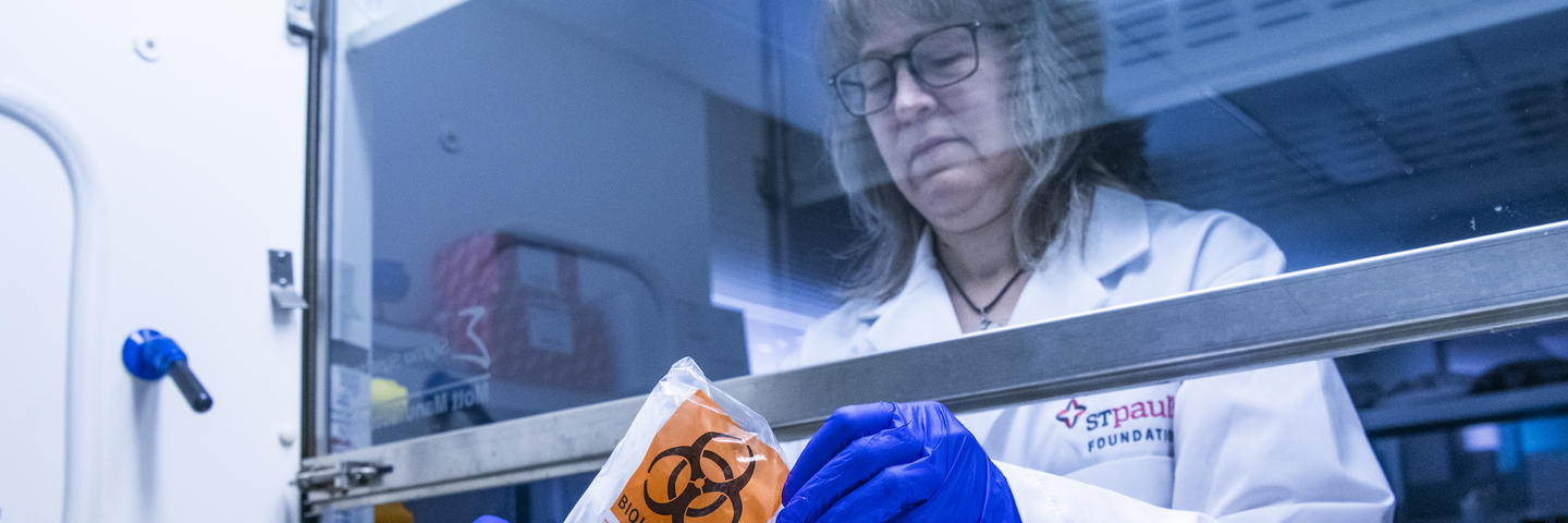 A woman in lab coat holds a biohazard bag