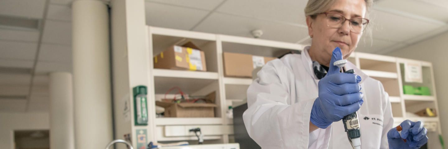 A woman in a lab coat stands in a lab working with lab equipment