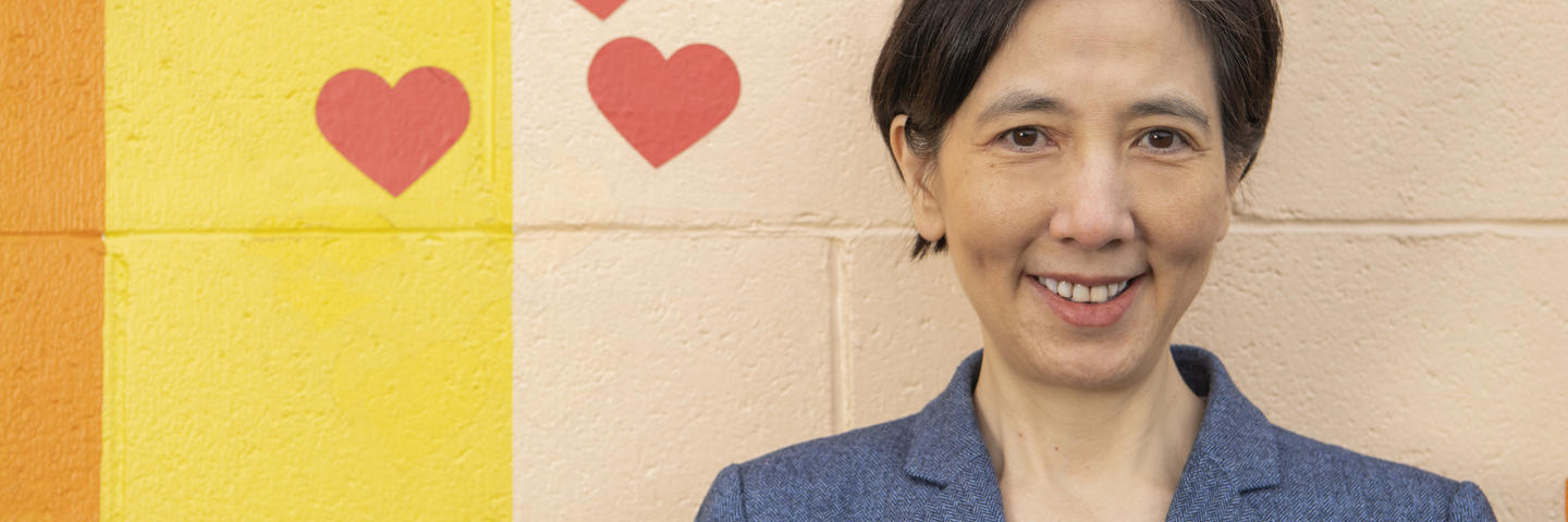 A woman stands in front of a colorful wall smiling at the camera